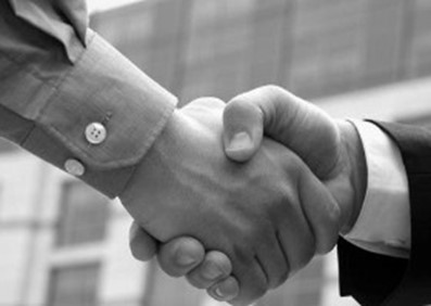 Black and white image of two hands shaking, symbolizing agreement or partnership, with a blurred office building in the background, conveying professionalism.