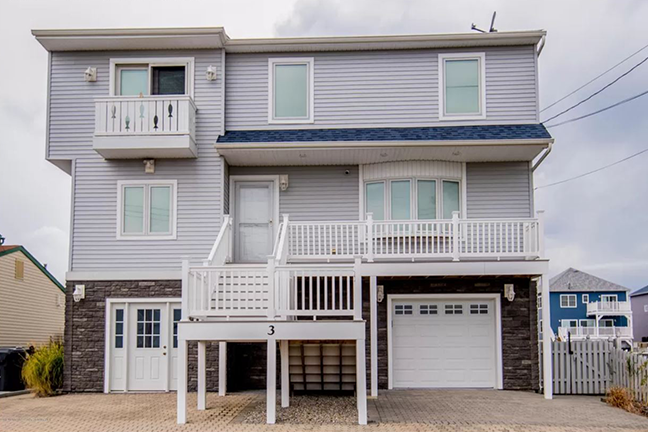 Two-story gray house with white trim and balconies. Features a garage and stone accents. Overcast sky adds a calm, subdued atmosphere.