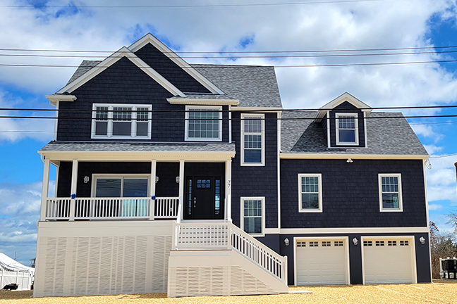 Two-story dark blue house with white trim, a covered porch, and a double garage. Cloudy sky and sunlight create a calm, inviting atmosphere.