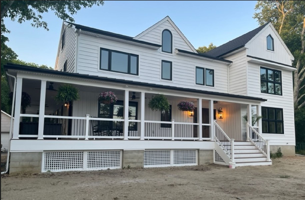 Two-story white house with black-framed windows, a porch with hanging plants, and warm lights creating a welcoming atmosphere. Stairs lead up to the entrance.