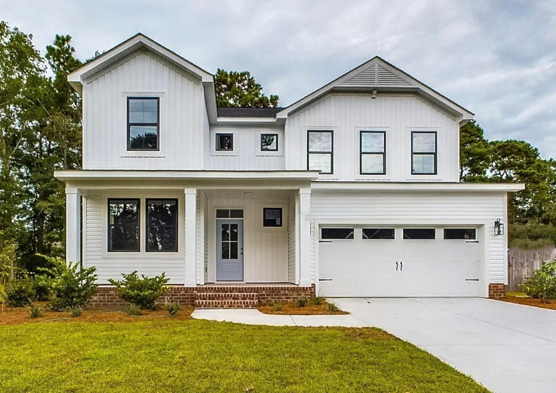 A modern two-story white house with a gable roof, large windows, and a two-car garage. It has a tidy lawn and a welcoming front porch under a cloudy sky.