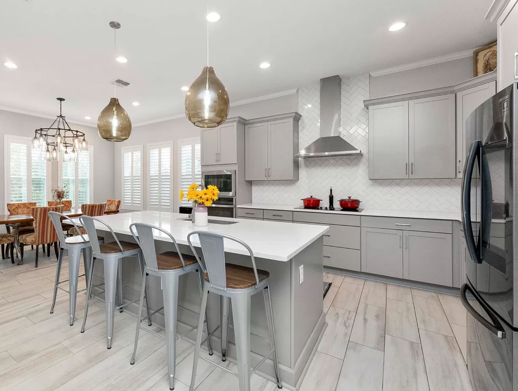 Modern kitchen with gray cabinets, large island, metal bar stools, and pendant lights. Bright, spacious, and contemporary with a welcoming feel.