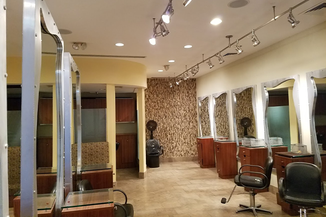 A modern hair salon with stylish brown chairs, mirrors, and a patterned wall. The space is well-lit with overhead lights, creating a clean, welcoming atmosphere.
