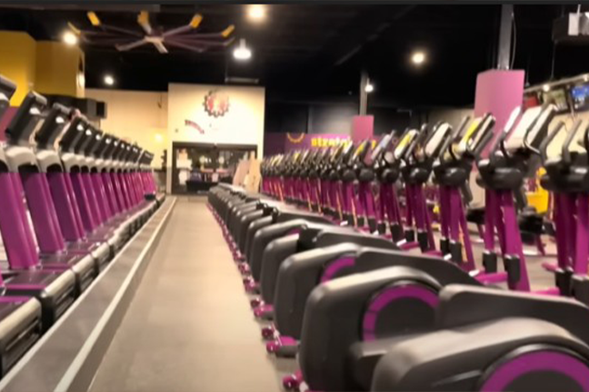 Row of treadmills in a gym, all in purple and black, under bright overhead lights. The setting is clean, organized, and ready for workout.