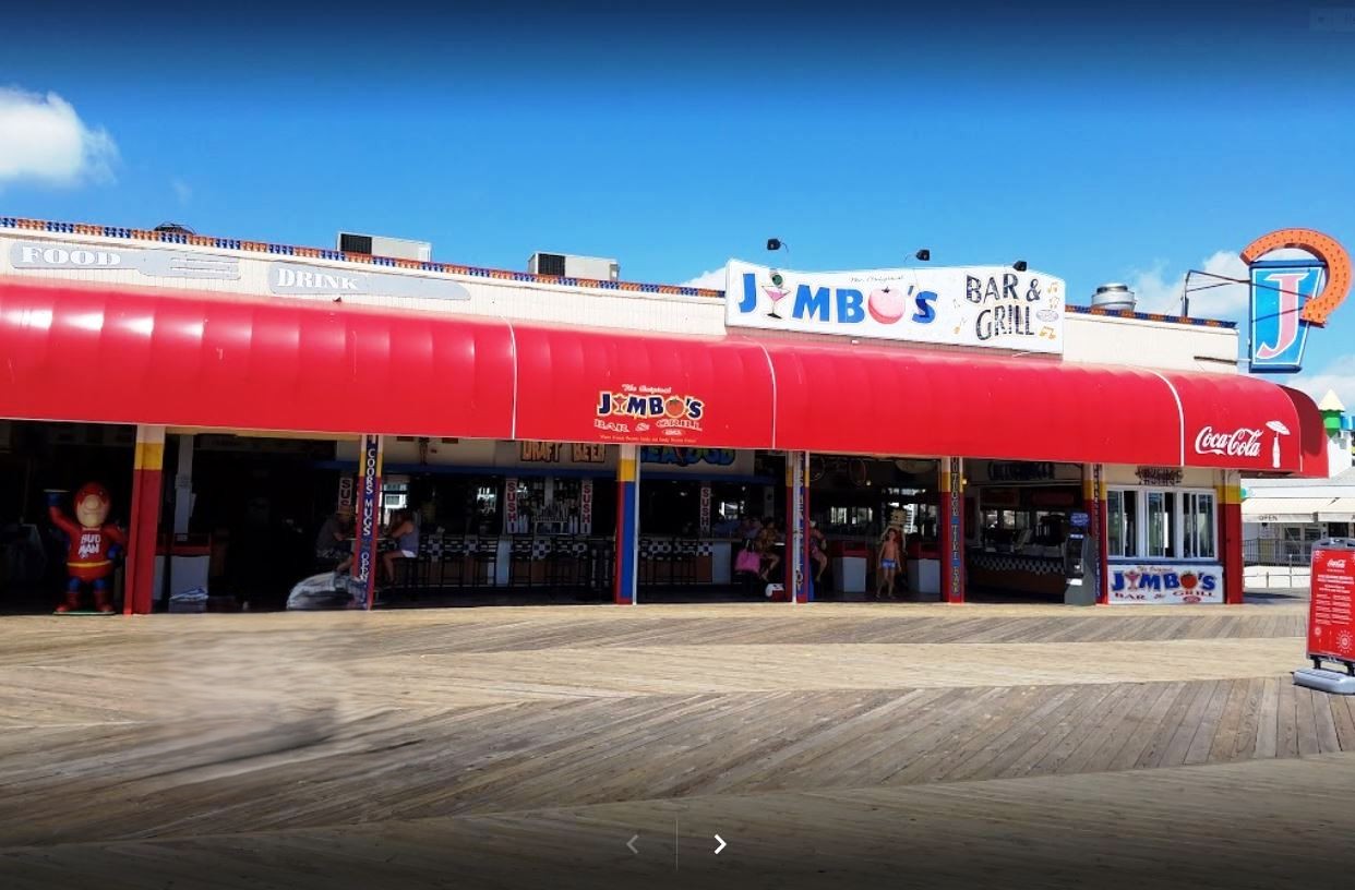A diner with a bright red awning and a retro sign reading "Jimbo's Bar & Grill" under a clear blue sky. The exterior has a classic, vintage vibe.