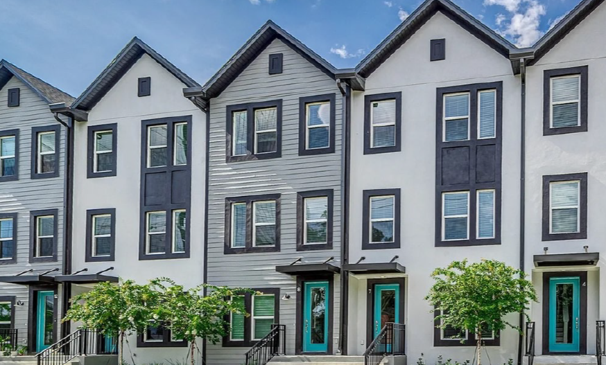 Modern townhouse exterior with three stories, gray siding, and black trim. Two teal front doors, windows symmetrically aligned, under a clear blue sky.