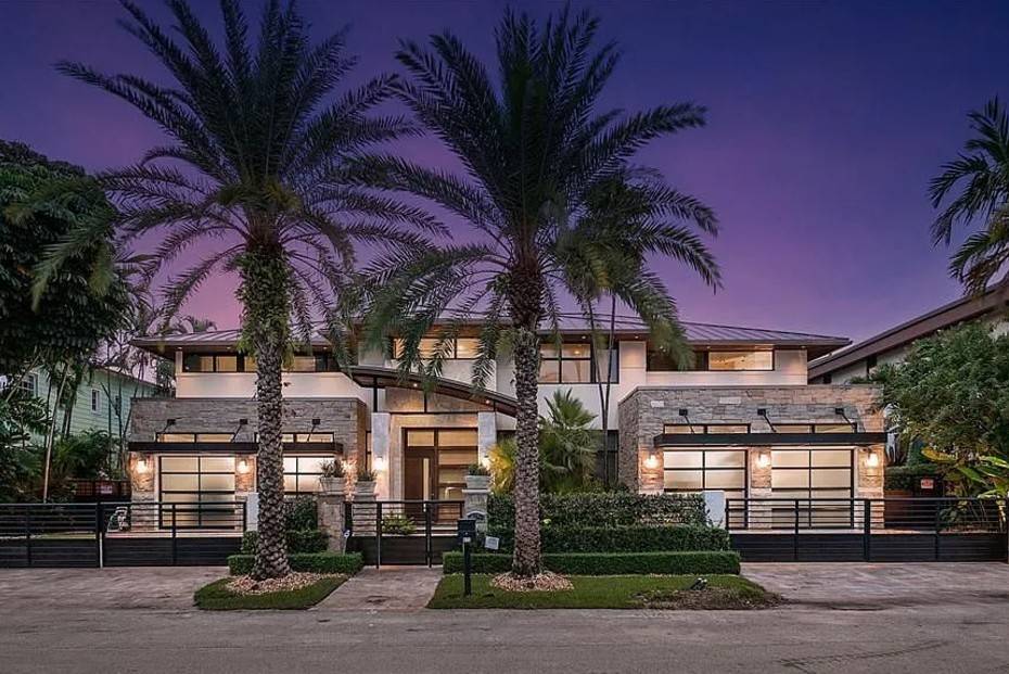 Modern house exterior at dusk with two tall palm trees in front, warm lighting from windows, and a purple sky in the background conveying elegance and tranquility.