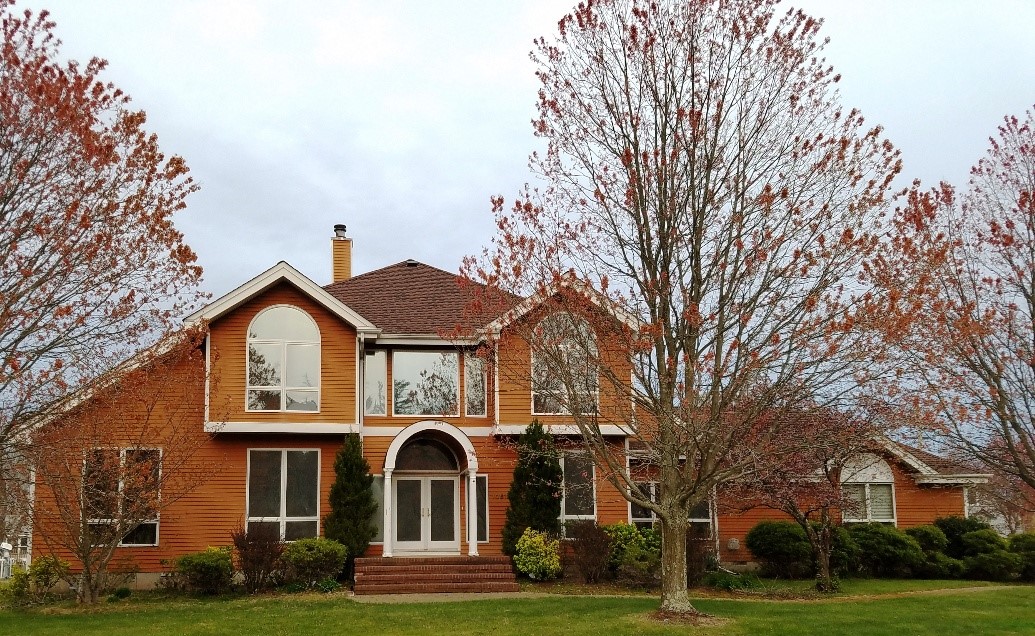 Two-story brick house with large arched windows and a wooden front door. A leafless tree stands in the front yard, conveying a calm, autumn atmosphere.