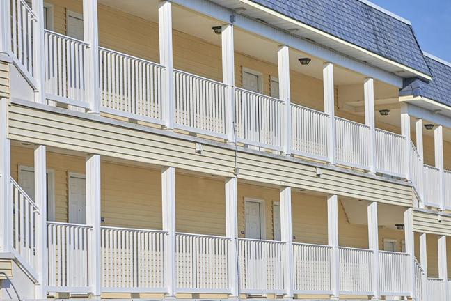 Three-story building with a row of white columns and railings on each floor's balcony. The facade is beige, exuding a neat, orderly appearance.