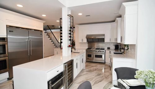 Modern kitchen with white cabinetry and marble-patterned floor. It features a stainless steel refrigerator, oven, wine rack, and sleek countertop.